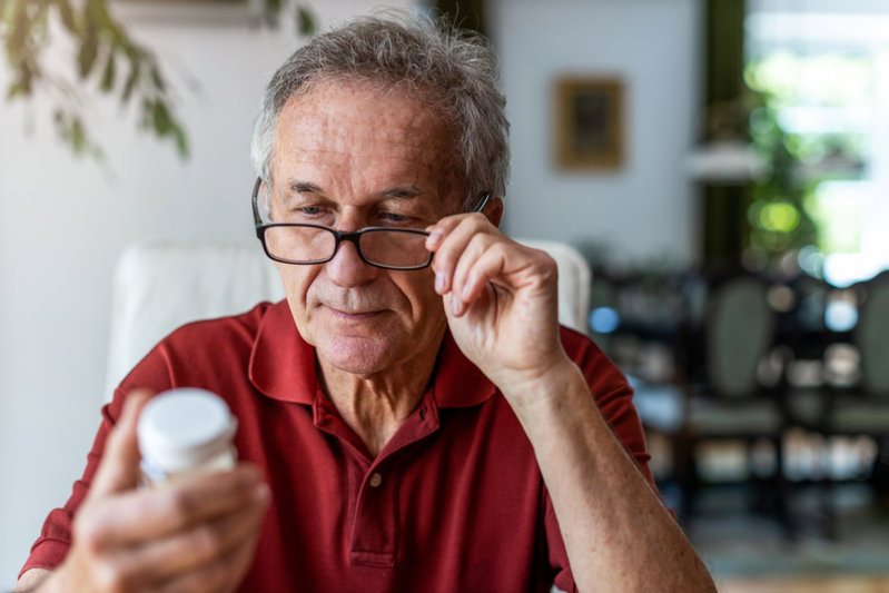 older man looking at bottle of pills
